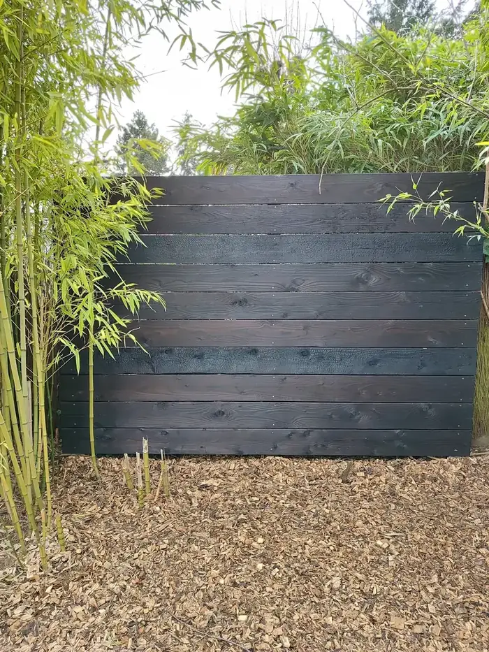 Clôture en bois brûlé noir installée devant des bambous